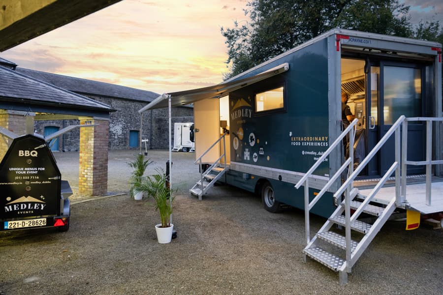Medley's branded mobile catering truck and BBQ trailer set up at sunset in a cobbled courtyard